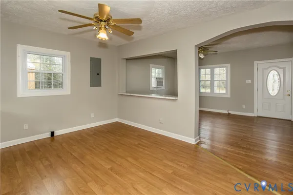 an empty room with wooden floor chandelier fan and windows