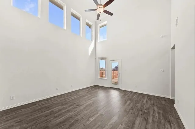 a view of an empty room with wooden floor and a ceiling fan