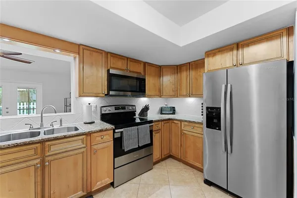 a kitchen with granite countertop a refrigerator a sink a stove a microwave and wooden cabinets
