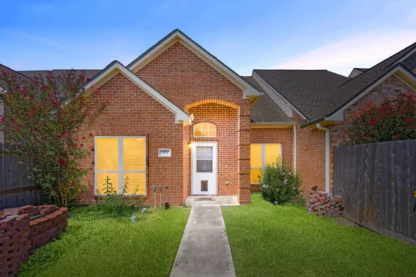 a view of a brick house with a large windows and a yard with plants and large trees