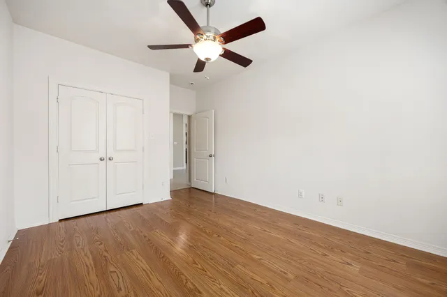 an empty room with wooden floor ceiling fan and windows