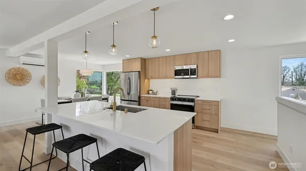 a kitchen with stainless steel appliances kitchen island granite countertop a stove a sink a microwave a dining table and chairs with wooden floor