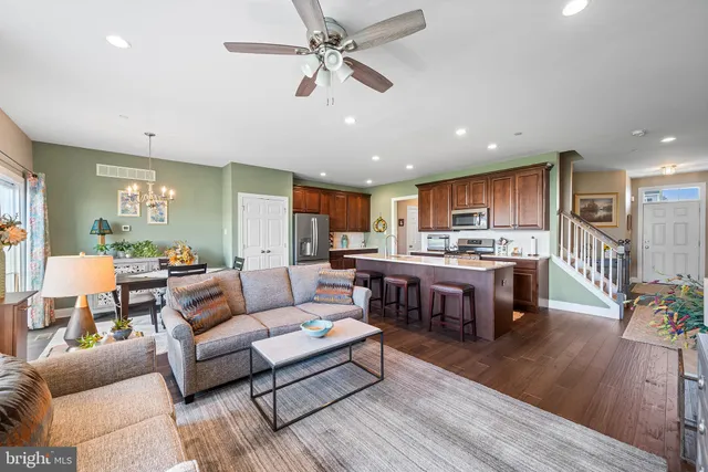 a kitchen with stainless steel appliances kitchen island granite countertop a refrigerator a stove a sink a dining table and chairs with wooden floor
