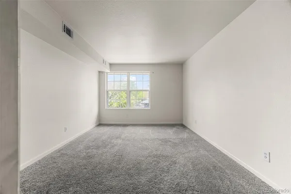 a view of an empty room with wooden floor and a kitchen