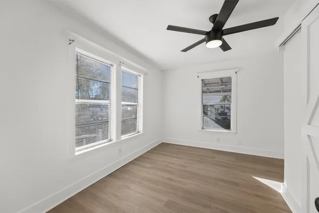 an empty room with wooden floor fan and windows