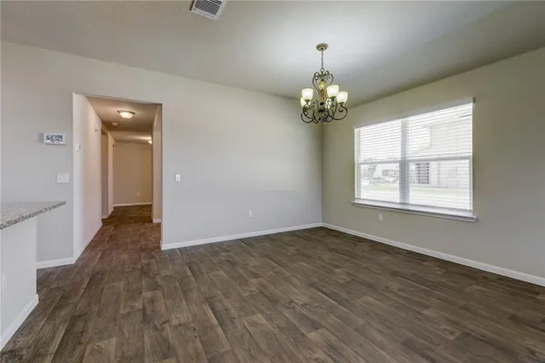 an empty room with wooden floor chandelier and windows