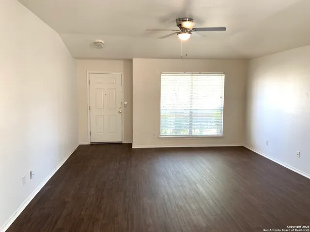 an empty room with wooden floor chandelier fan and windows
