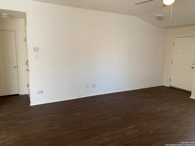 a view of an empty room with wooden floor and a chandelier fan