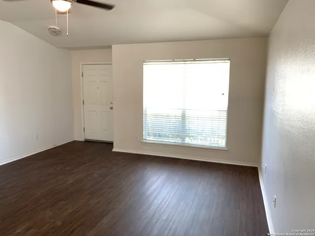 an empty room with wooden floor chandelier fan and windows