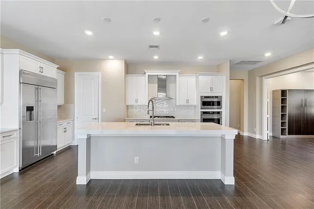 a kitchen with stainless steel appliances granite countertop a sink stove a refrigerator and white cabinets with wooden floor