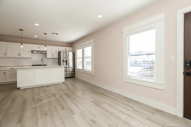 a large white kitchen with kitchen island a sink wooden floor and a large window