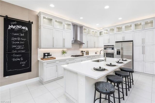 a kitchen with stainless steel appliances kitchen island granite countertop a sink a stove a refrigerator and white cabinets with wooden floor