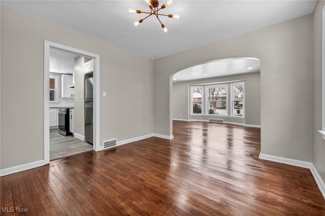 13614 Cedar Road Cleveland, OH 44118 - Photo 7 of 46 Unfurnished living room with arched walkways, a notable chandelier, wood finished floors, visible vents, and baseboards