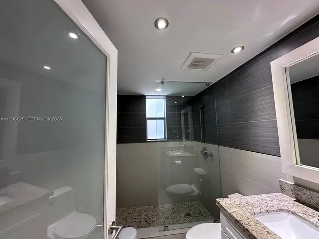 a bathroom with a granite countertop sink a toilet a mirror and shower