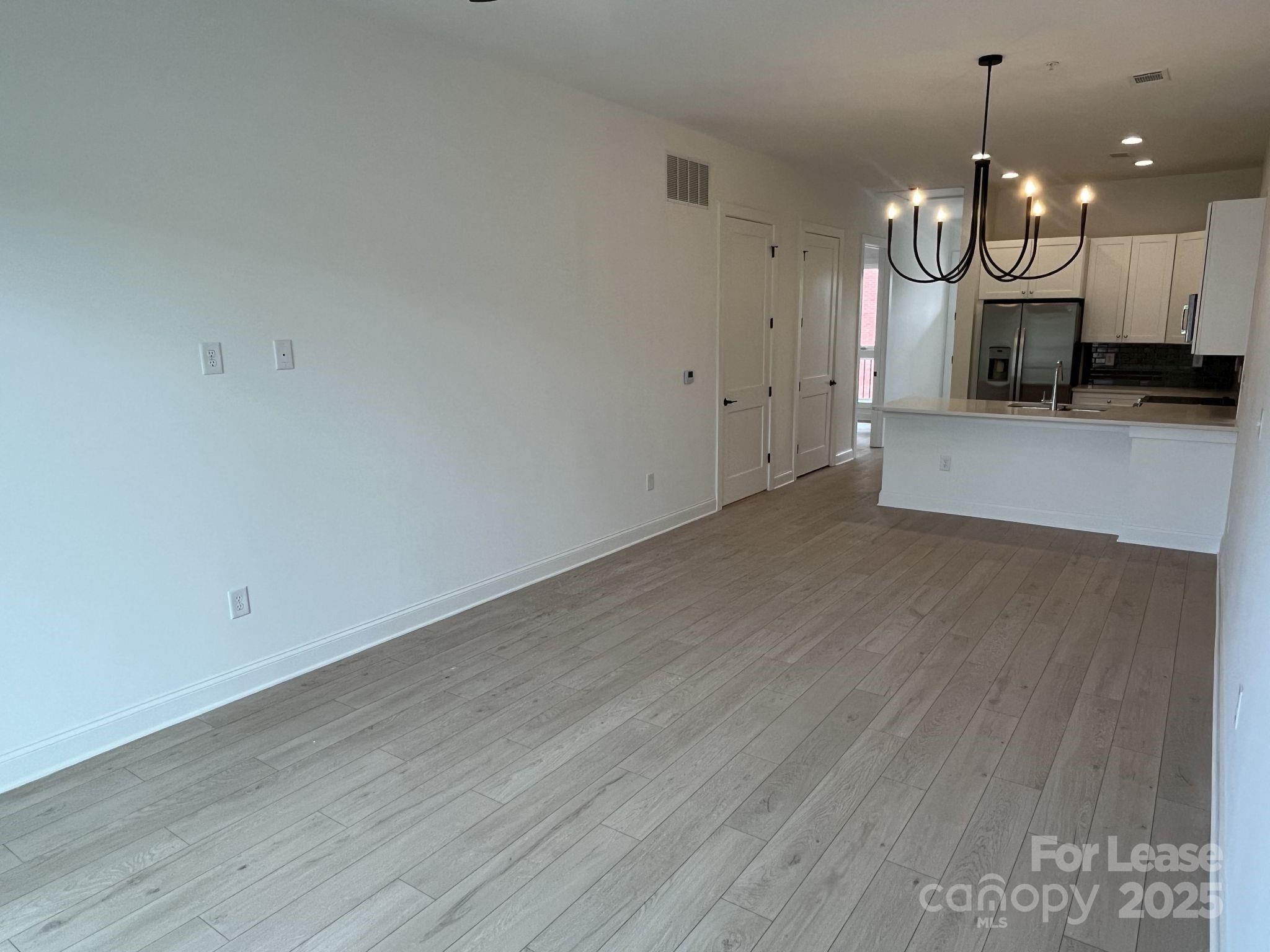 19546 Greentree Way, Unit 203 Cornelius, NC 28031 - Photo 17 of 32 an empty room with wooden floor and kitchen view