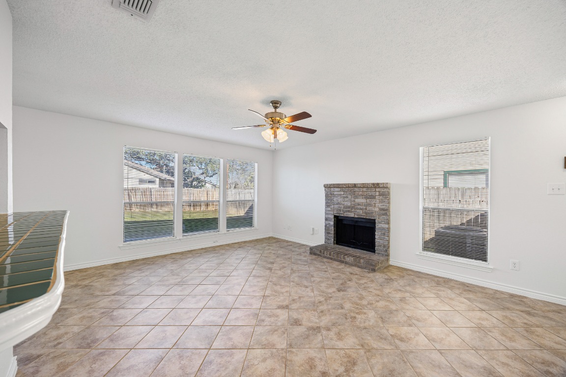 2630 Alcott Lane, Unit A Austin, TX 78748 - Photo 8 of 32 Unfurnished living room featuring a fireplace with raised hearth, a textured ceiling, plenty of natural light, ceiling fan, and light tile patterned floors