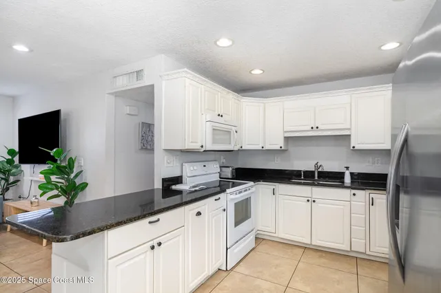 a kitchen with granite countertop white cabinets white appliances and potted plant