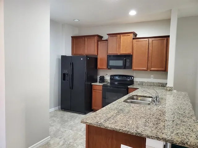 a kitchen with granite countertop wooden cabinets a refrigerator and a sink