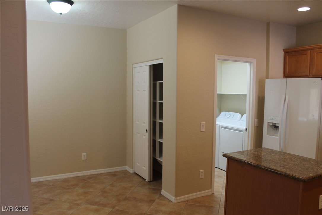 7352 Ravines Avenue Las Vegas, NV 89131 - Photo 44 of 93 Kitchen with white refrigerator with ice dispenser, brown cabinetry, light tile patterned flooring, a kitchen island, and independent washer and dryer