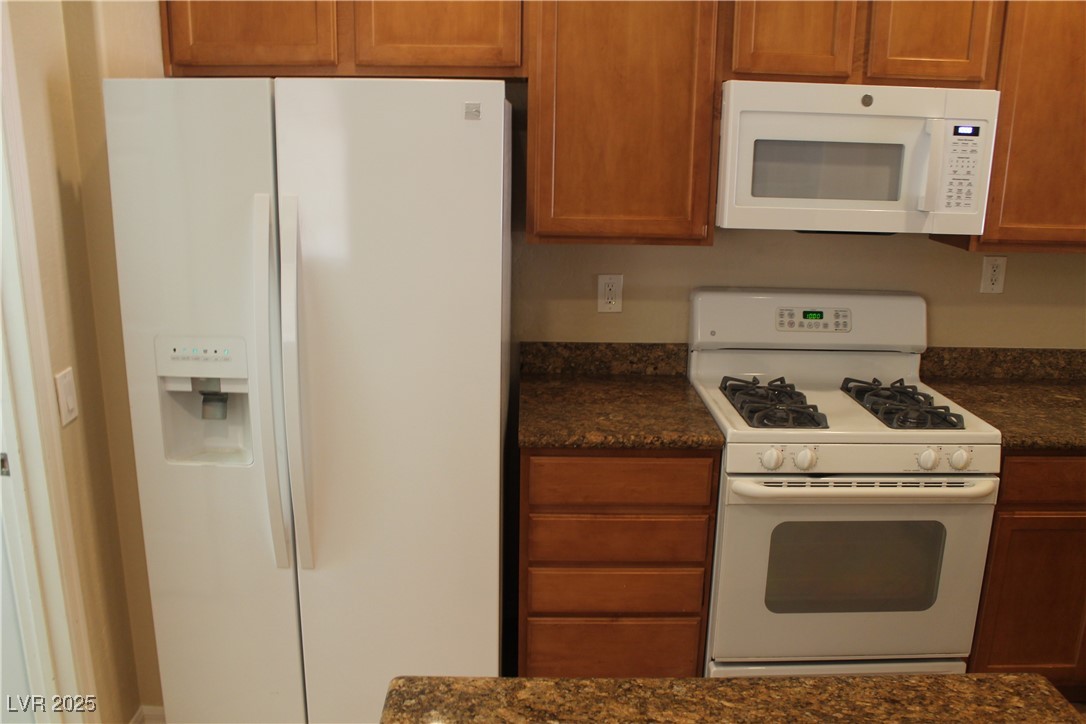 7352 Ravines Avenue Las Vegas, NV 89131 - Photo 9 of 93 Kitchen with white appliances, brown cabinets, and dark stone counters