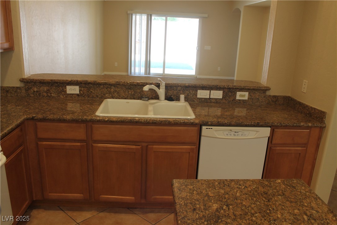 7352 Ravines Avenue Las Vegas, NV 89131 - Photo 10 of 93 Kitchen with dishwasher, dark stone countertops, light tile patterned floors, and brown cabinets