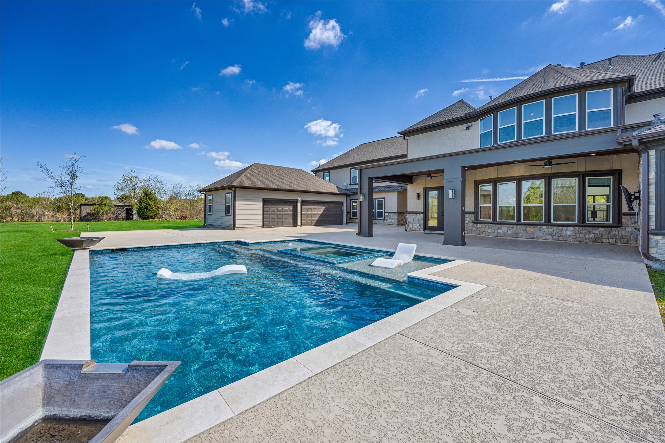 15015 House Road Cypress, TX 77433 - Photo 10 of 50 This photo showcases a spacious backyard with a modern swimming pool, ample patio space, and a large covered outdoor area. The home features a sleek exterior design with multiple windows for natural light and a detached garage, set against a backdrop of open greenery. Perfect for entertaining and relaxation.