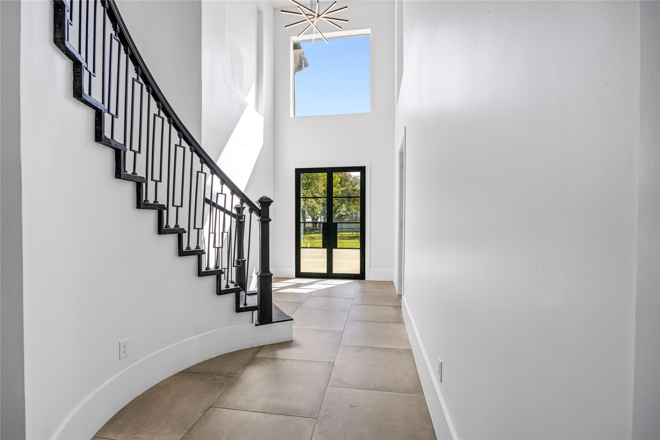 15015 House Road Cypress, TX 77433 - Photo 12 of 50 This photo showcases a modern, bright entryway with a high ceiling and large window, allowing natural light to illuminate the space. The elegant, sweeping staircase features a sleek black railing, and the neutral tile flooring complements the minimalist design.