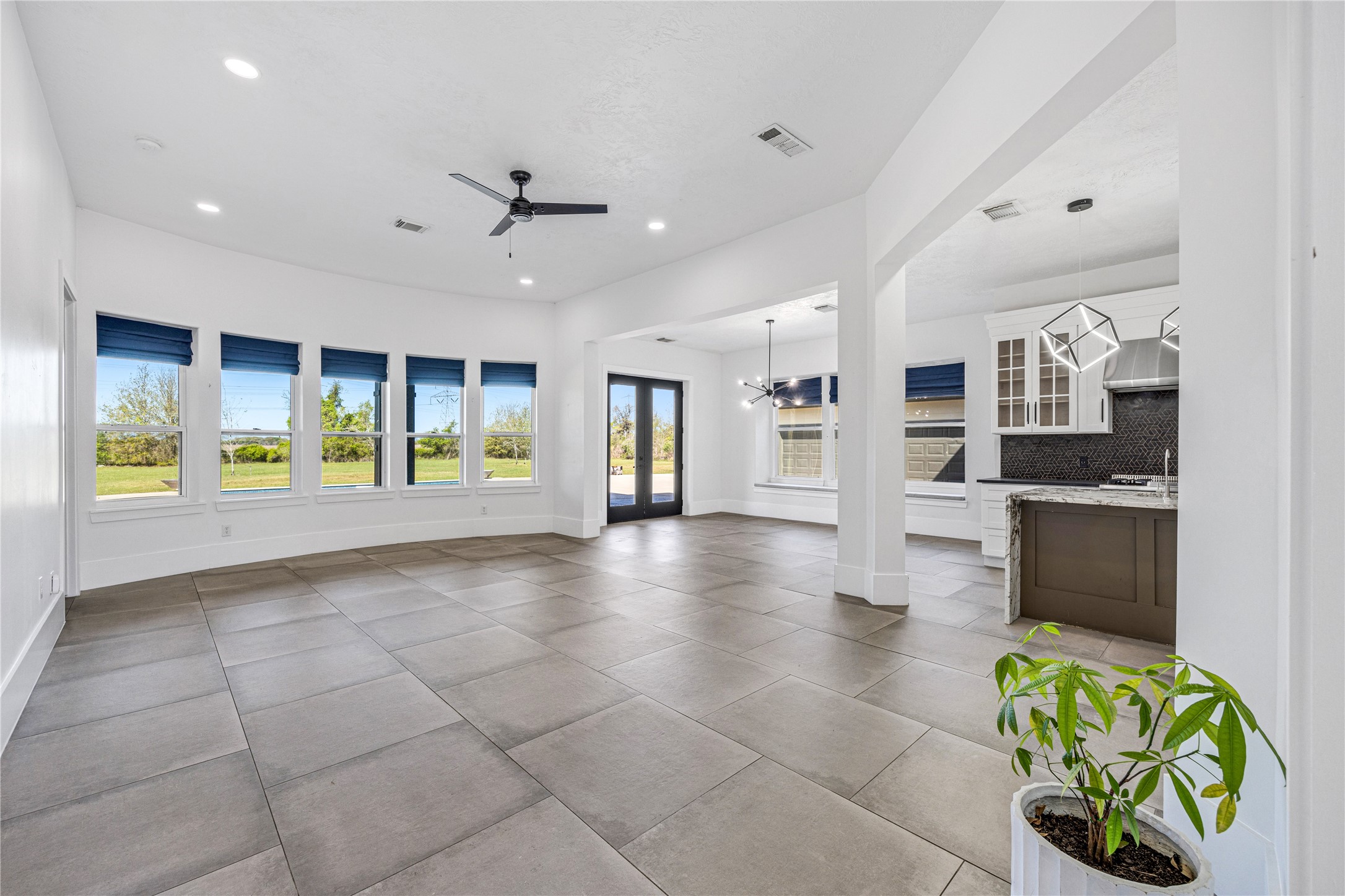 15015 House Road Cypress, TX 77433 - Photo 13 of 50 This spacious, open-concept living area features large tile flooring, abundant natural light from expansive windows, a modern ceiling fan, and access to a sleek kitchen with contemporary lighting and fixtures. Ideal for comfortable living and entertaining.
