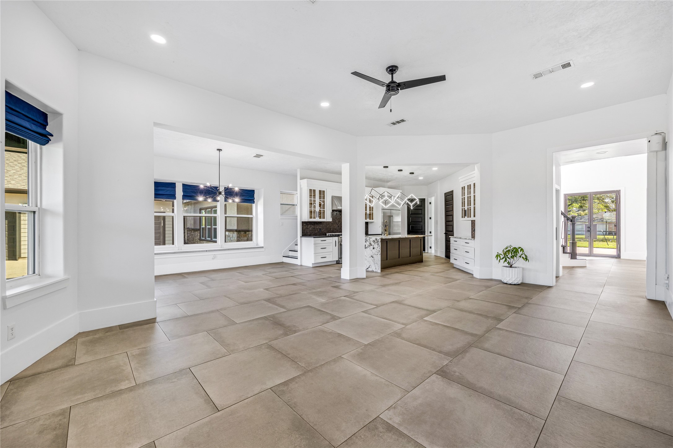 15015 House Road Cypress, TX 77433 - Photo 14 of 50 This spacious open-concept living area features large floor tiles, abundant natural light, and a modern ceiling fan. The adjacent kitchen boasts sleek cabinetry and a stylish island. Large windows and glass doors enhance the airy feel, leading to a lovely outdoor view.