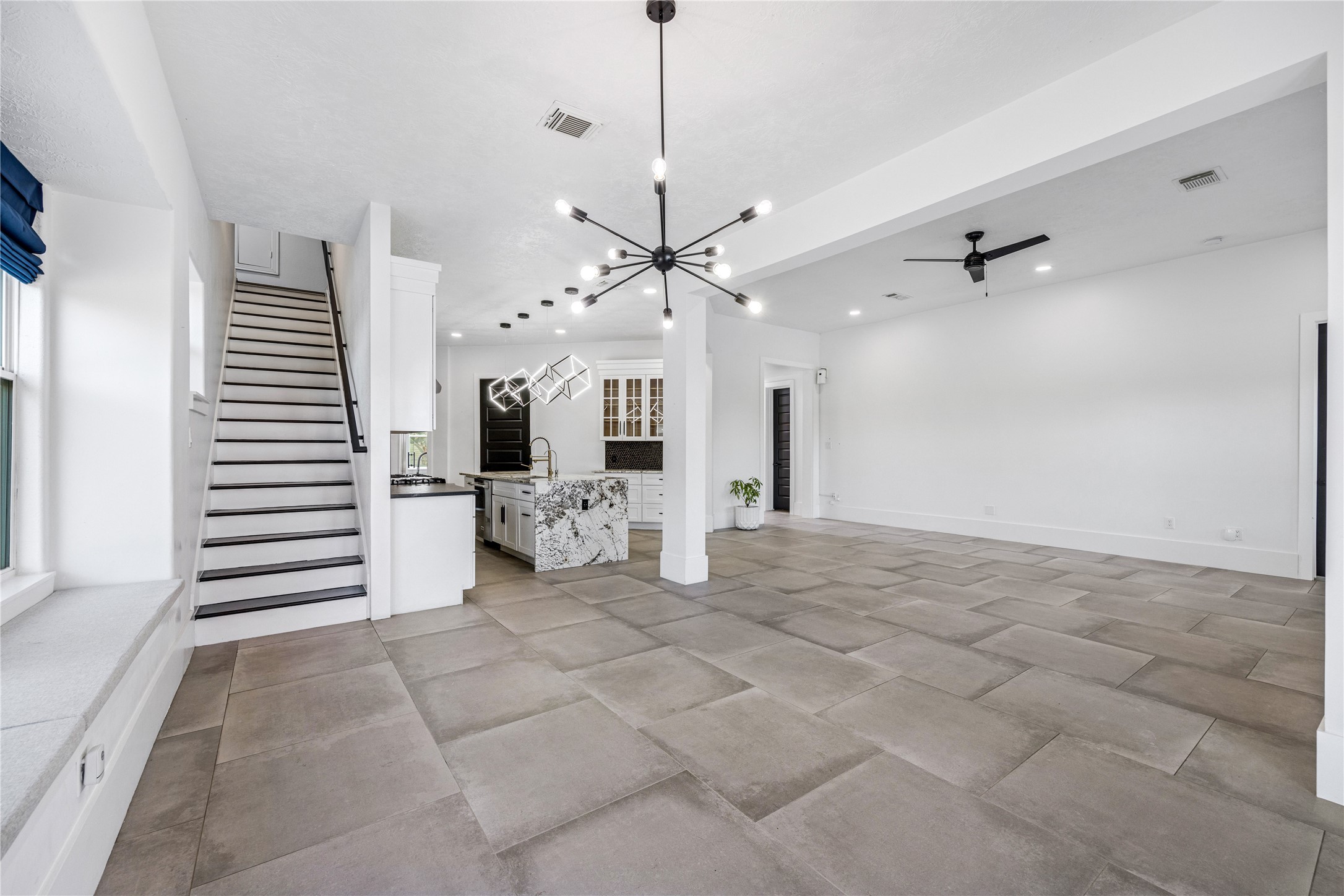 15015 House Road Cypress, TX 77433 - Photo 15 of 50 This open-concept living space features large tile flooring, modern lighting fixtures, and a spacious kitchen with a stylish island. A staircase leads to the upper level, and there's ample natural light from large windows.