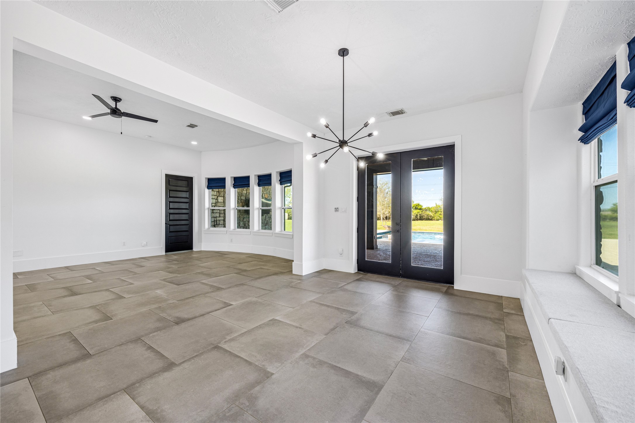 15015 House Road Cypress, TX 77433 - Photo 16 of 50 This spacious room features large floor tiles, a modern light fixture, and ample natural light from multiple windows and glass doors leading to a patio. The neutral palette and contemporary design create a welcoming atmosphere.