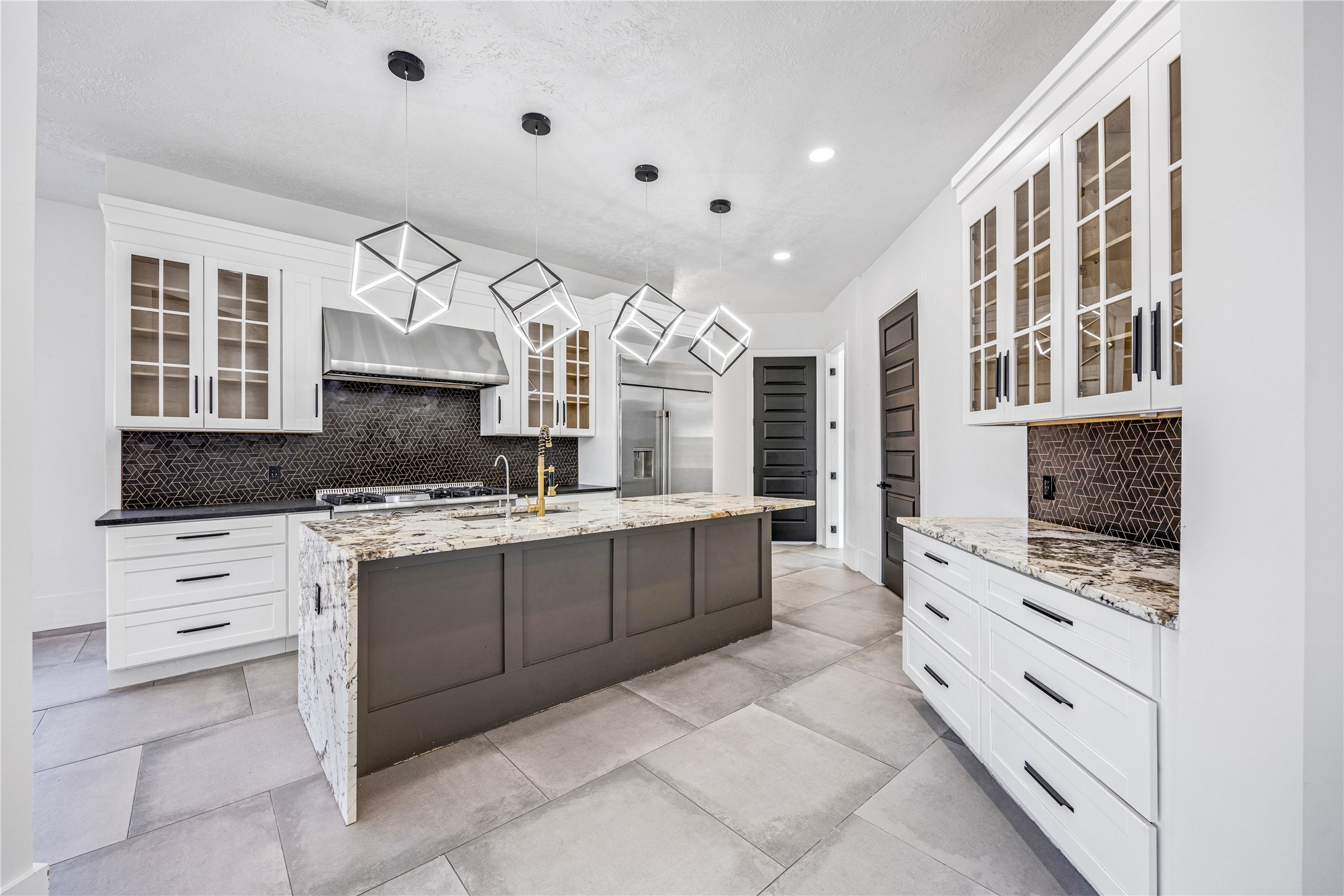 15015 House Road Cypress, TX 77433 - Photo 18 of 50 Modern kitchen with sleek cabinetry, a large central island with granite countertops, and unique geometric pendant lighting. Features stainless steel appliances, dark tile backsplash, and ample storage with glass-front cabinets.