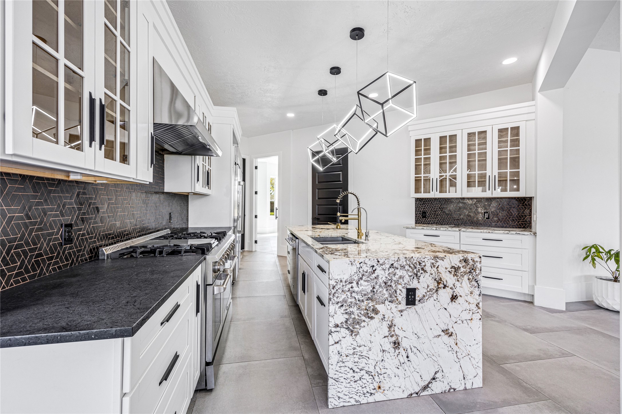 15015 House Road Cypress, TX 77433 - Photo 19 of 50 This modern kitchen features sleek white cabinetry with glass-front doors, a striking black geometric backsplash, and an elegant marble island. It offers stainless steel appliances, contemporary pendant lighting, and ample counter space, creating a stylish and functional culinary space.