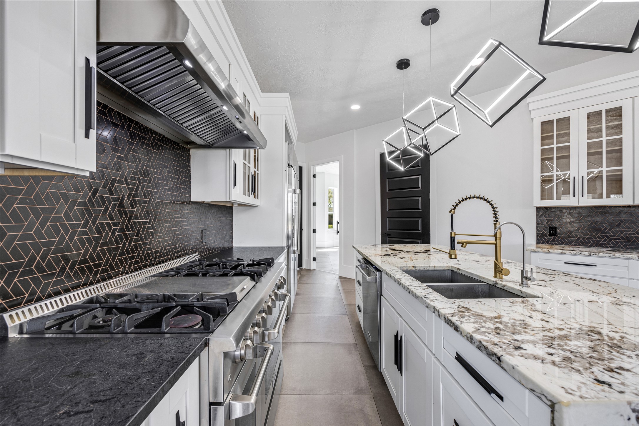 15015 House Road Cypress, TX 77433 - Photo 20 of 50 This modern kitchen features sleek white cabinetry, a striking black geometric backsplash, and a spacious granite countertop island with a built-in sink. It includes a high-end gas stove and contemporary pendant lighting, creating a stylish and functional cooking space.