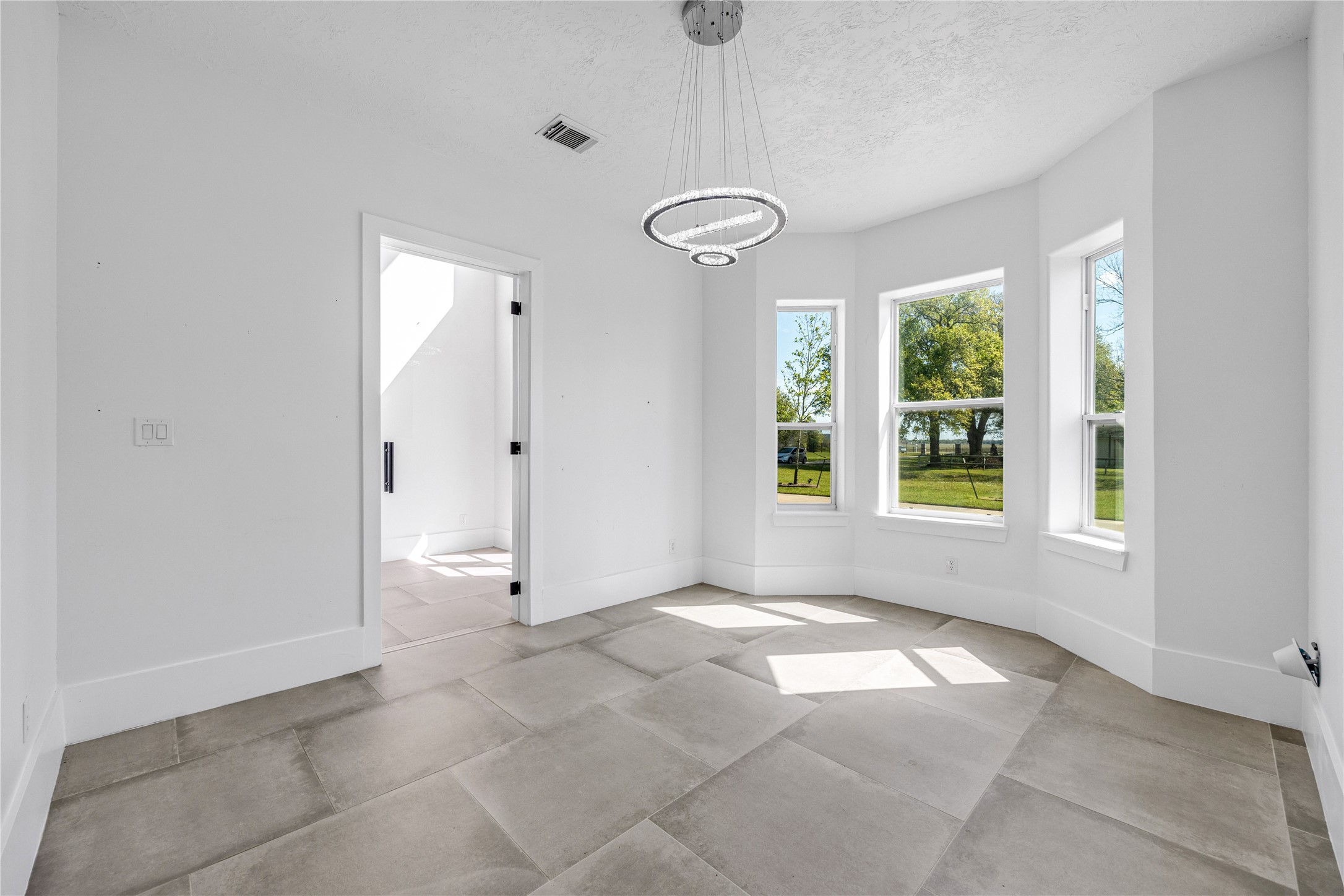 15015 House Road Cypress, TX 77433 - Photo 25 of 50 Bright room with large floor tiles, bay windows offering scenic greenery views, and a modern circular light fixture. Fresh white walls enhance the spacious feel. Suitable for a cozy sitting area or home office.