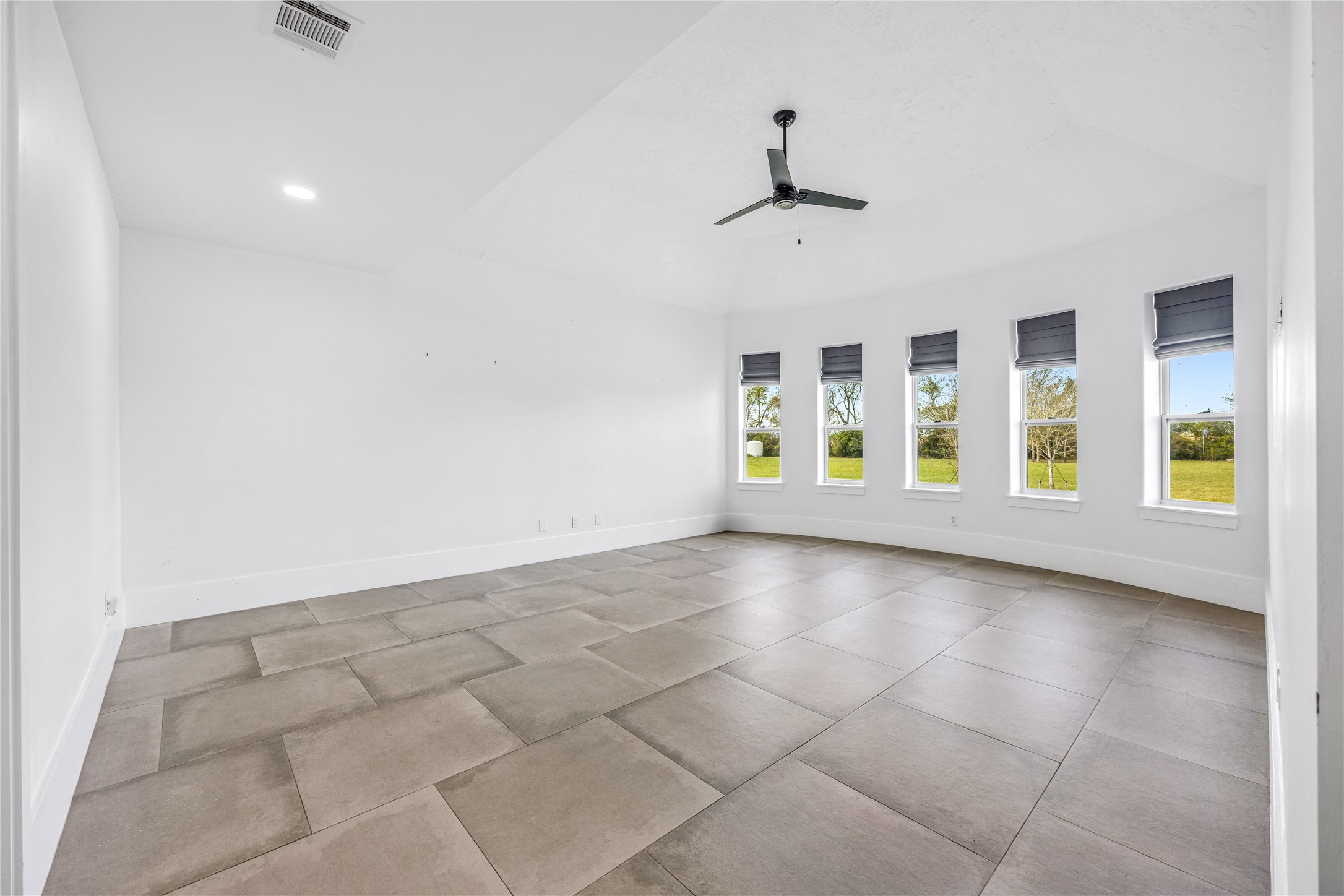 15015 House Road Cypress, TX 77433 - Photo 26 of 50 This spacious, primary light-filled room features large floor tiles, a ceiling fan, and multiple windows with views of a grassy outdoor area. Perfect for a bright and airy living space.