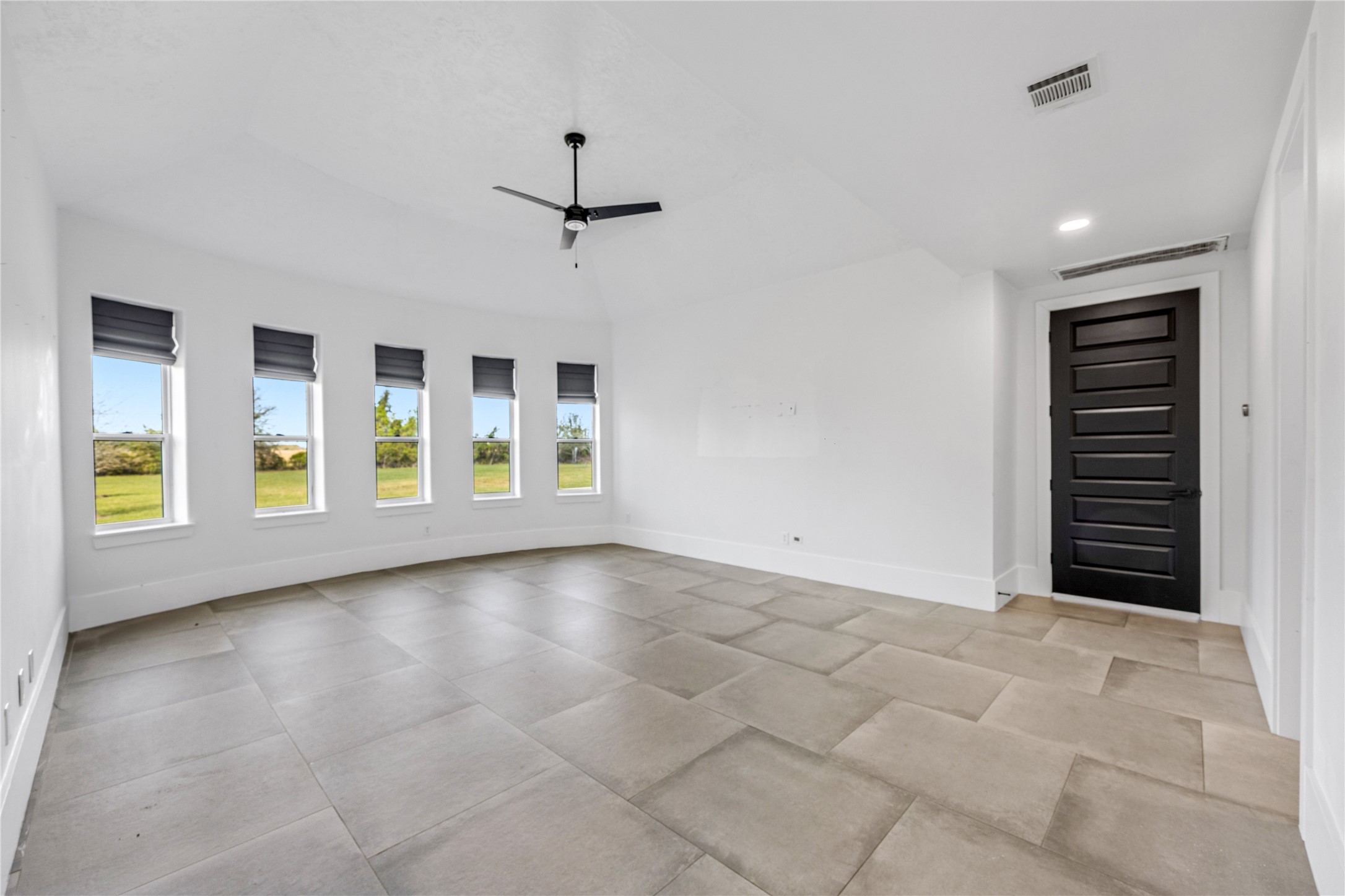 15015 House Road Cypress, TX 77433 - Photo 27 of 50 This spacious, bright room features large windows with outdoor views, a sleek ceiling fan, modern tile flooring, and a stylish black door, offering a clean and contemporary feel.