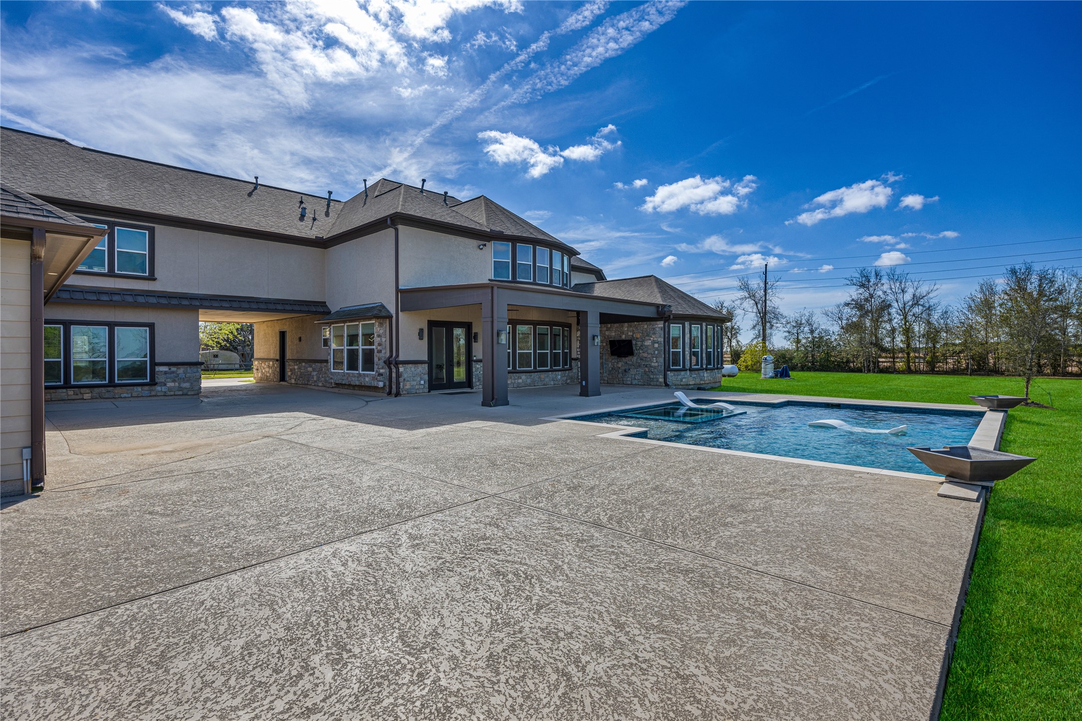 15015 House Road Cypress, TX 77433 - Photo 3 of 50 This photo showcases a spacious, modern home with a large backyard featuring a sleek swimming pool. The exterior is a mix of stone and siding, with ample windows for natural light. The patio area is expansive, ideal for outdoor activities and entertaining.