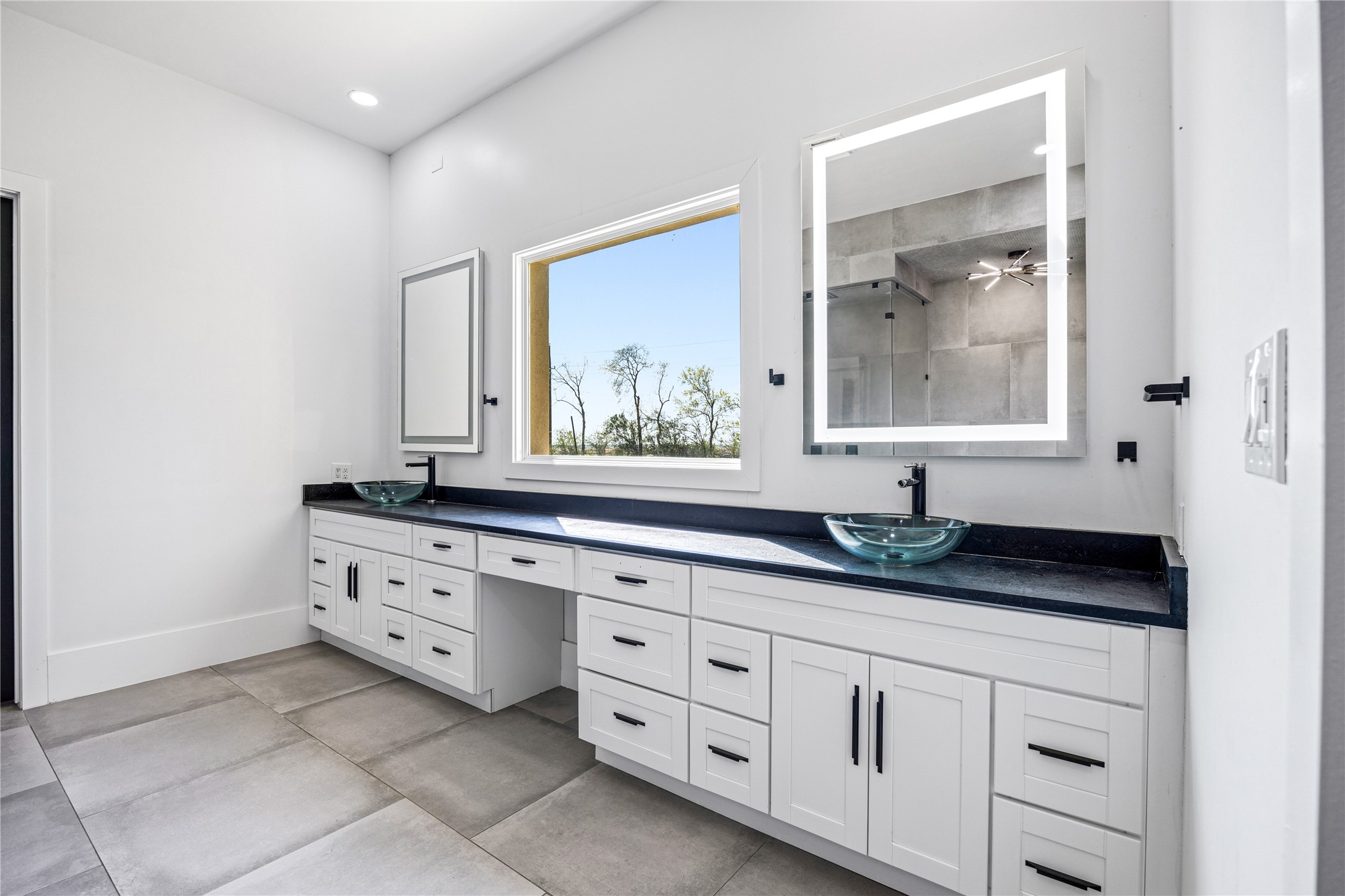 15015 House Road Cypress, TX 77433 - Photo 29 of 50 This modern bathroom features dual vanities with vessel sinks, illuminated mirrors, and ample cabinetry. A large window provides natural light, complementing the sleek design and spacious layout.