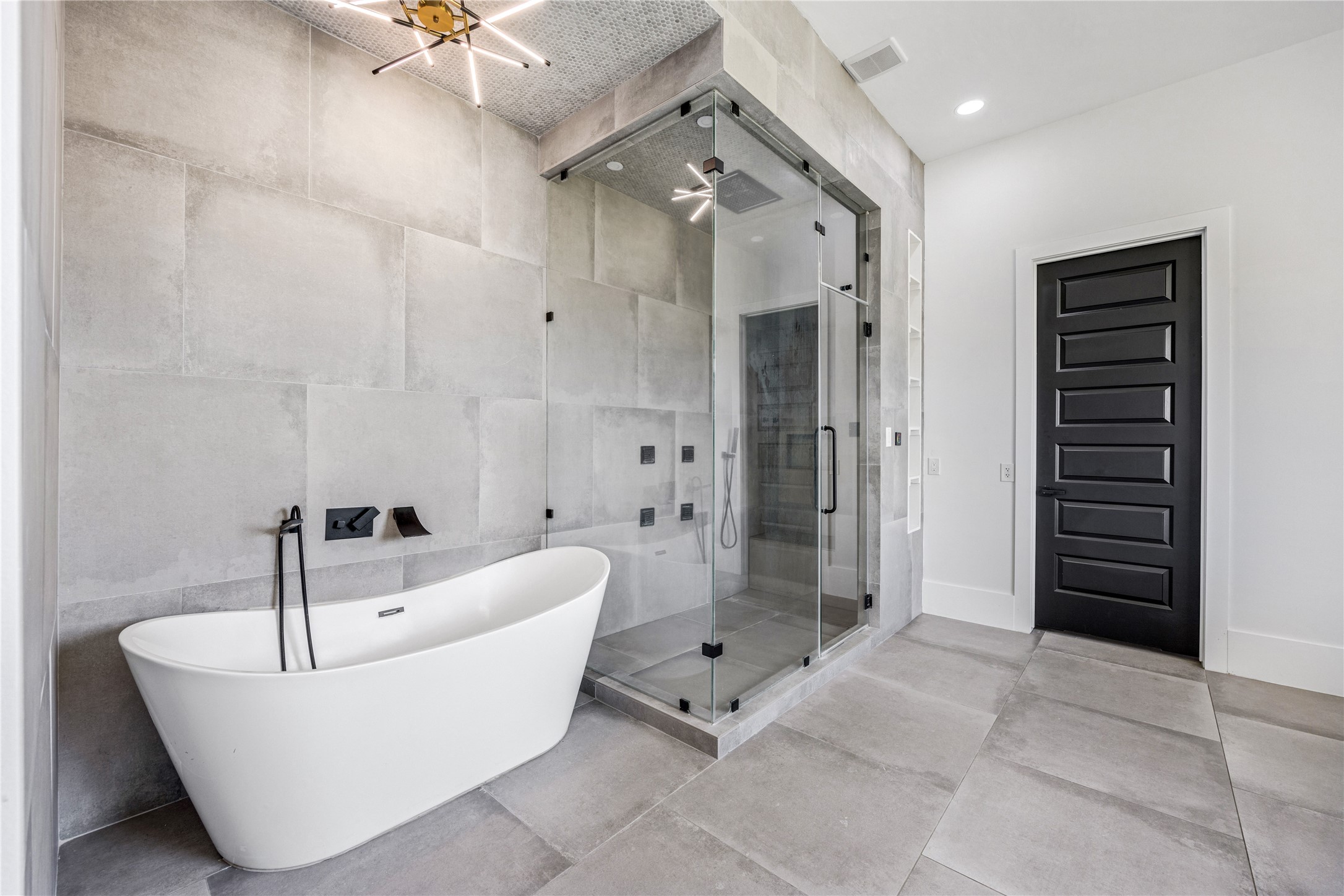 15015 House Road Cypress, TX 77433 - Photo 30 of 50 This modern bathroom features a sleek freestanding bathtub and a spacious glass-enclosed shower. The large tiles and contemporary lighting create a clean, elegant look, complemented by a stylish black door.
