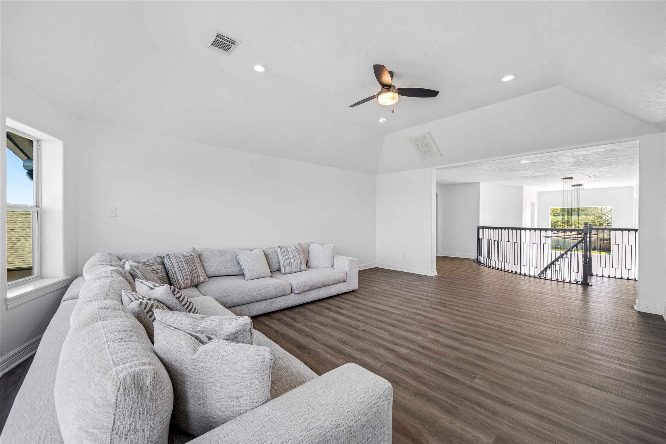 15015 House Road Cypress, TX 77433 - Photo 33 of 50 Spacious living area with high ceilings, featuring a modern ceiling fan and recessed lighting. The room has wood-style flooring and a large, comfortable sectional sofa. An open railing provides a view to the lower level, enhancing the airy feel.