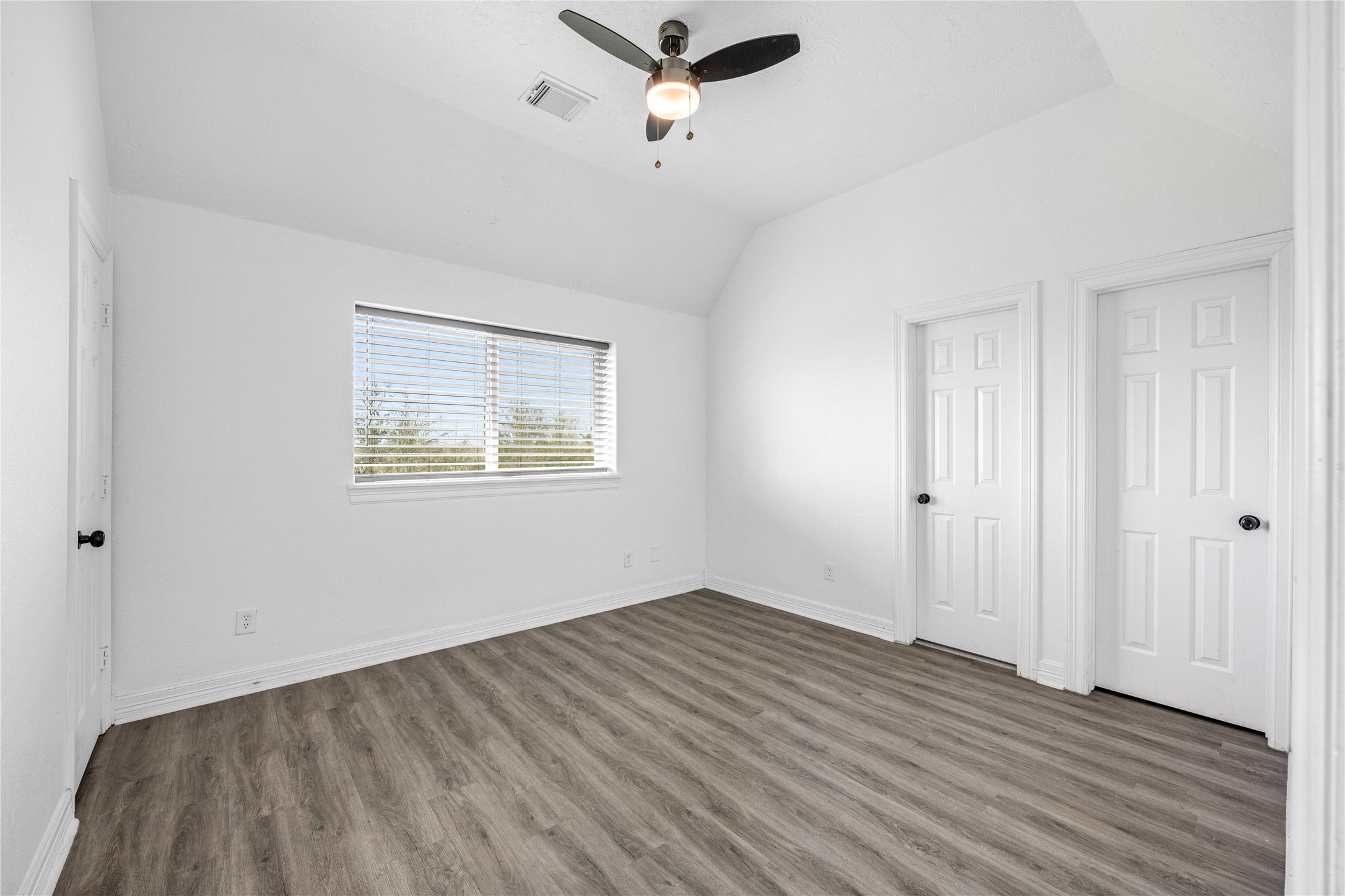 15015 House Road Cypress, TX 77433 - Photo 35 of 50 Bright, spacious room with a vaulted ceiling, featuring a window with blinds, modern ceiling fan, and wood-look flooring. Two doors provide additional access and storage options.