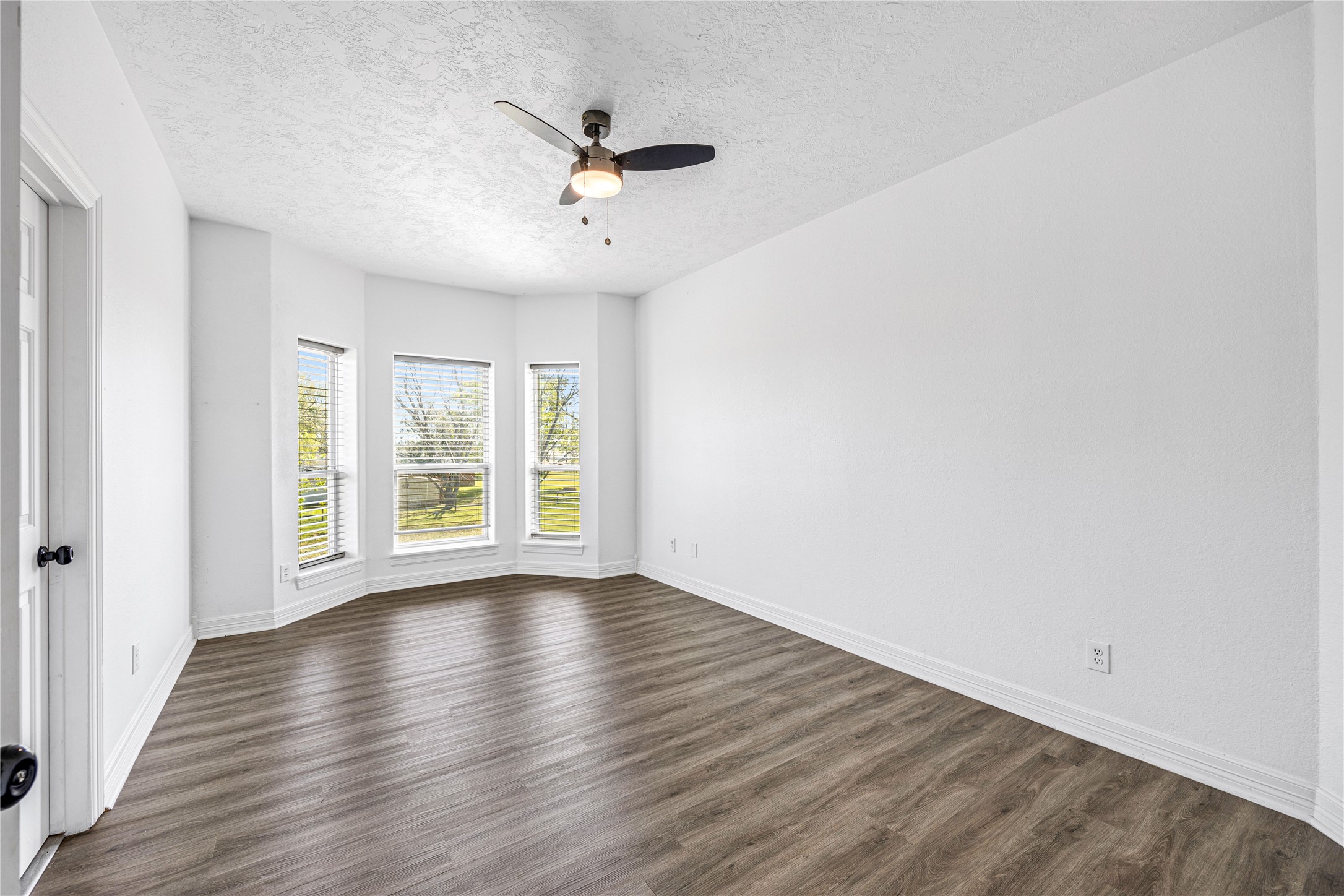 15015 House Road Cypress, TX 77433 - Photo 36 of 50 This photo shows a bright, spacious room with large bay windows, providing plenty of natural light. It features modern wood flooring and a ceiling fan, creating a comfortable and inviting atmosphere.