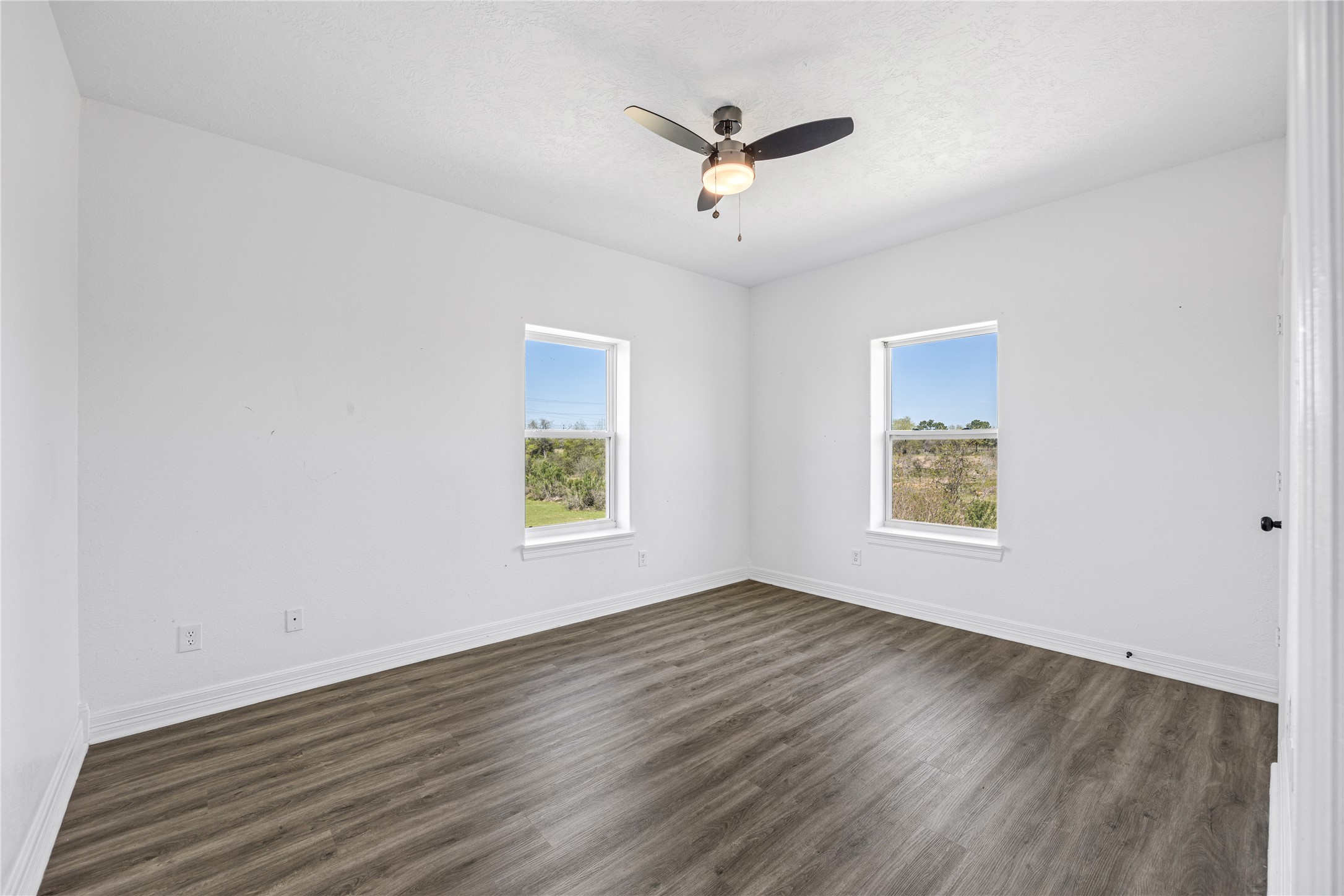 15015 House Road Cypress, TX 77433 - Photo 40 of 50 This photo showcases a bright, minimalistic room with white walls and wood-look flooring. It features two windows allowing natural light and a ceiling fan for comfort.
