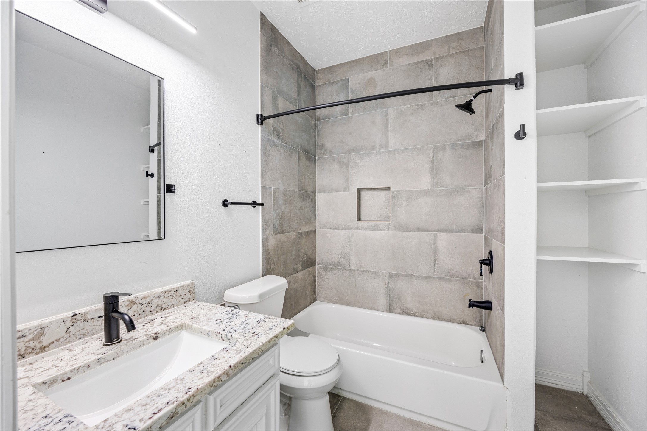 15015 House Road Cypress, TX 77433 - Photo 41 of 50 This modern bathroom features a sleek design with a tiled shower and bathtub, elegant granite countertop, and open shelving for storage. The neutral tones and black fixtures create a contemporary and inviting atmosphere.