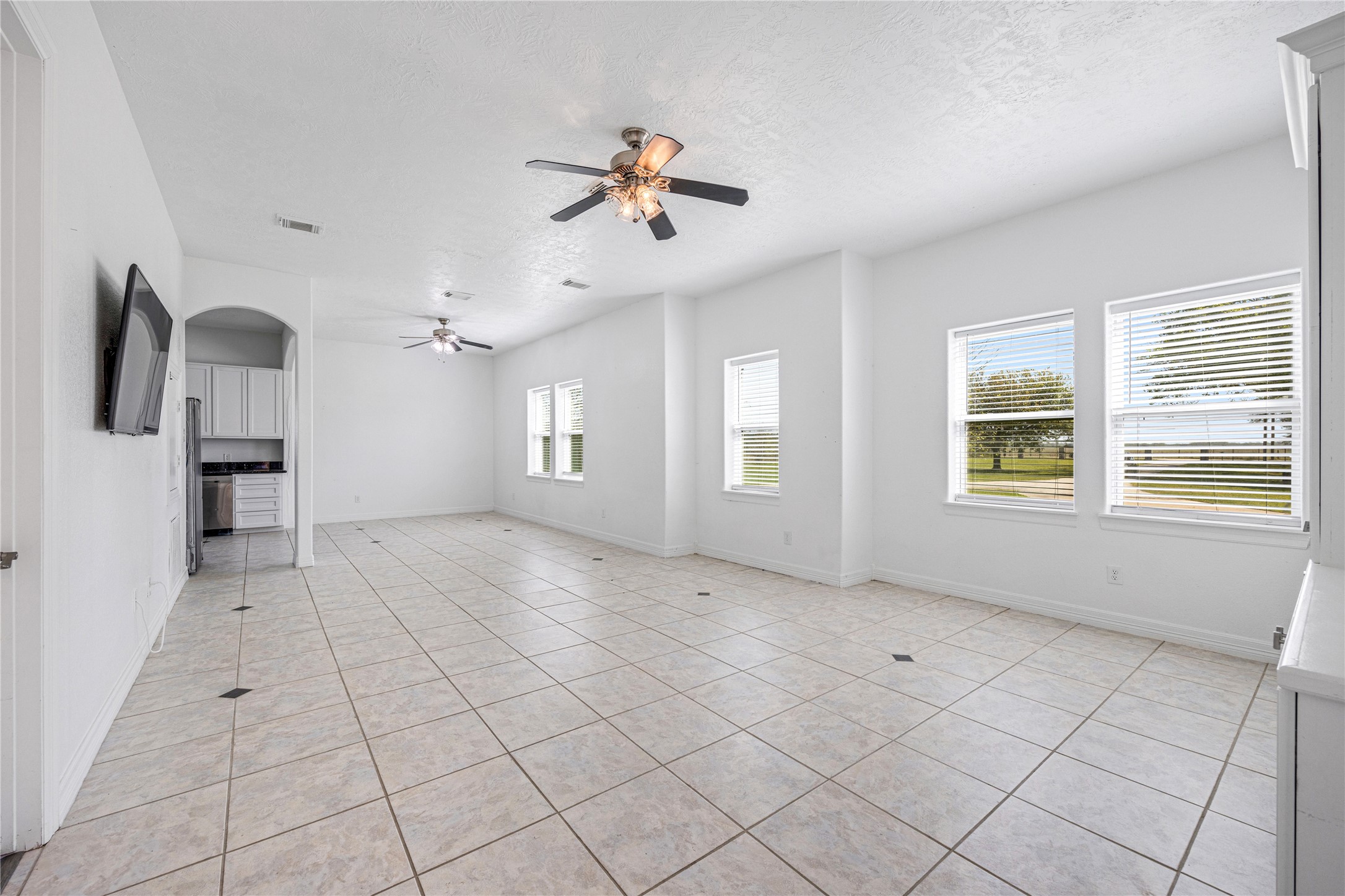 15015 House Road Cypress, TX 77433 - Photo 45 of 50 This bright, spacious living area features large windows for ample natural light, tiled flooring, and ceiling fans. It leads into a kitchen area with a visible archway, offering an open and airy atmosphere.