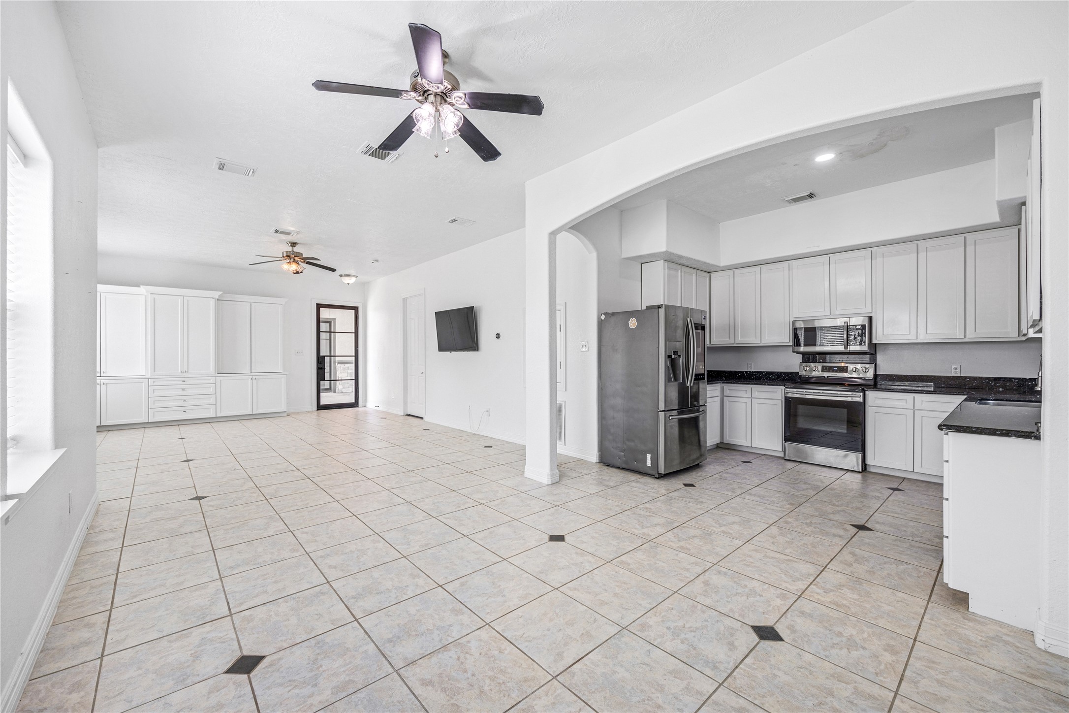 15015 House Road Cypress, TX 77433 - Photo 46 of 50 This spacious, open-concept kitchen and living area features sleek tile flooring, modern stainless steel appliances, ample cabinetry, and ceiling fans, providing a bright and functional space ideal for entertaining and family gatherings.Bright, spacious kitchen with modern stainless steel appliances, sleek white cabinetry, and contrasting black granite countertops. The tile flooring adds a clean, durable touch. Ideal for cooking and entertaining.