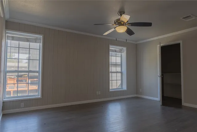 an empty room with wooden floor chandelier fan and windows