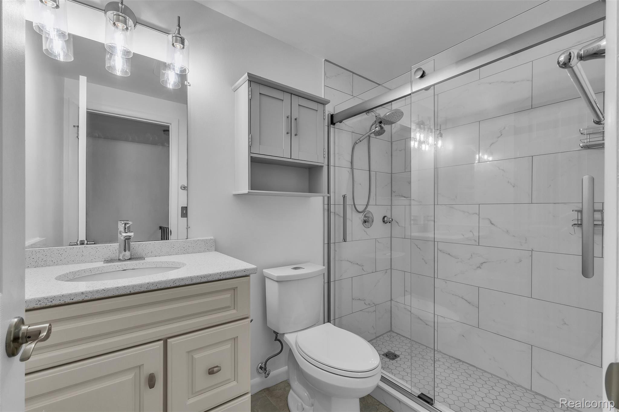 7000 Woonsocket Street Canton, MI 48187 - Photo 41 of 65 Bathroom featuring a glass-enclosed shower with tile surround and hex tile floor, a vanity with a white countertop and integrated sink, and an overhead lighting fixture