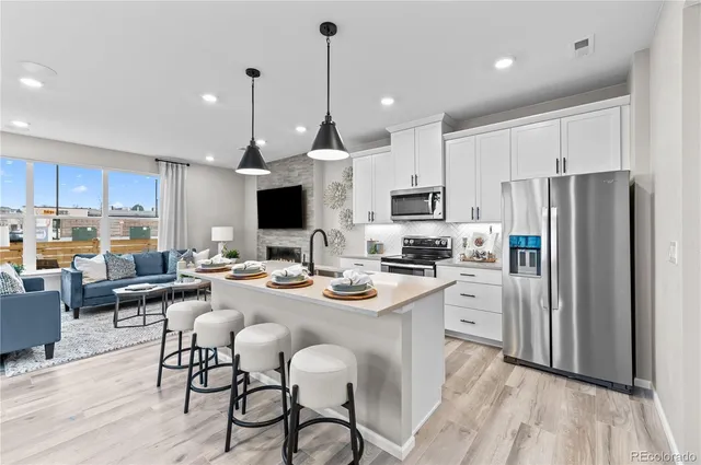 a kitchen with stainless steel appliances kitchen island granite countertop a refrigerator a stove a sink a island with chairs and wooden floor